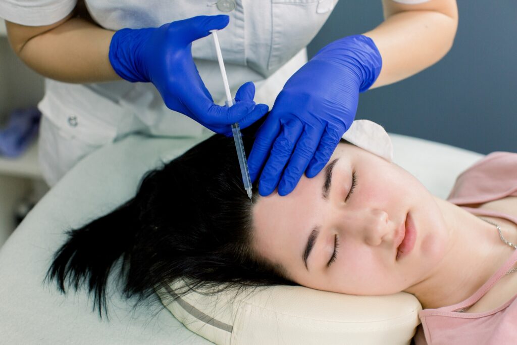 Hair mesotherapy or hair transplant: a beautician doctor makes injections in the head of a woman for hair growth or to prevent baldness.